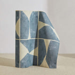 A curved partition stands on the ground, covered in a geometric grid print in blue-gray and cream.