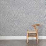 Wooden chair against wallpaper with small scale coral design in navy blue on white. 