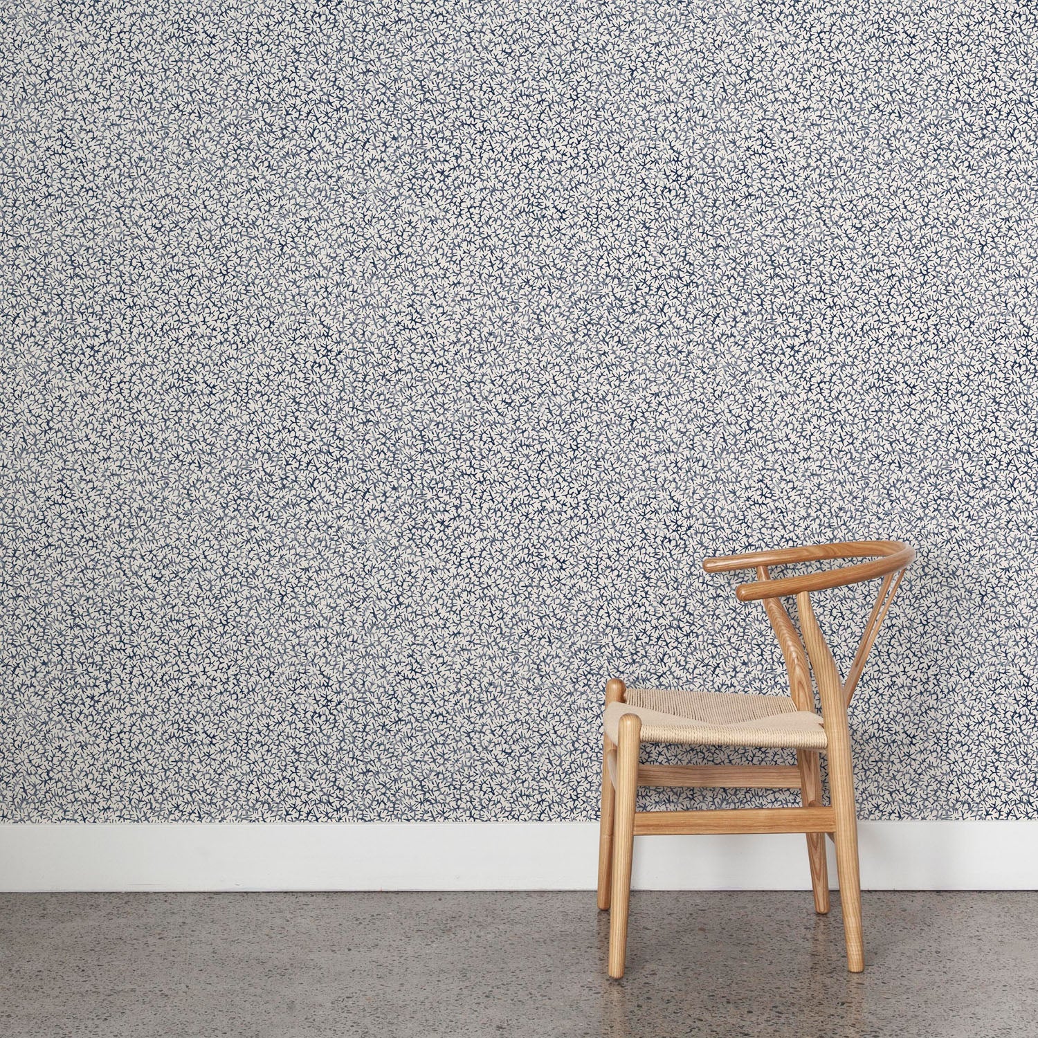 Wooden chair against wallpaper with small scale coral design in navy blue on white. 