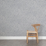 Wooden chair against wallpaper with small scale coral design in navy blue on white. 
