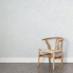 Wooden chair against a patterned pastel blue wallpaper wall