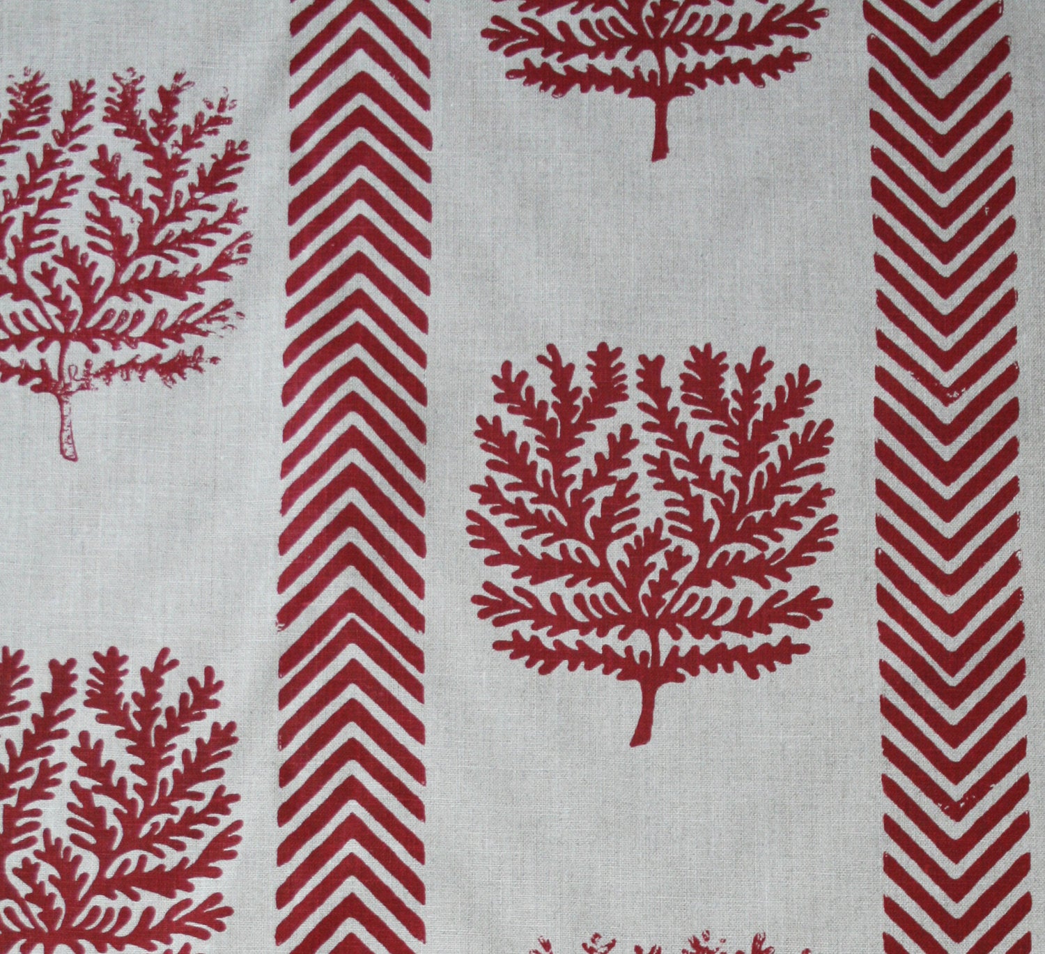 Detail of fabric in a in a tree and chevron stripe print in red on a white field.