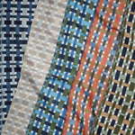 A close-up of patterned fabric swatches arranged diagonally, showing woven geometric designs in blue, navy, beige, green, orange, and white.