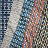 A close-up of patterned fabric swatches arranged diagonally, showing woven geometric designs in blue, navy, beige, green, orange, and white.