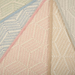 Stack of broadloom carpets in a dimensional herringbone stripe pattern in an array of pastel colors. 