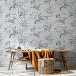 A bench and basket stand in front of a wall papered in a playful hand-drawn animal print in shades of blue on a white field.