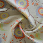 Close up of gently draped printed fabric with a whimsical floral pattern in blue, yellow and orange with dark brown stems on a soft blue background. 