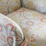 Close-up of a upholstered armchair with rolled arms and a cream fabric covered in a multicolor floral and vine pattern.