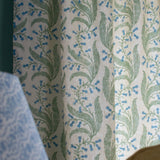 Detail of a curtain in a scrolling floral pattern in blue and green on a cream field. 