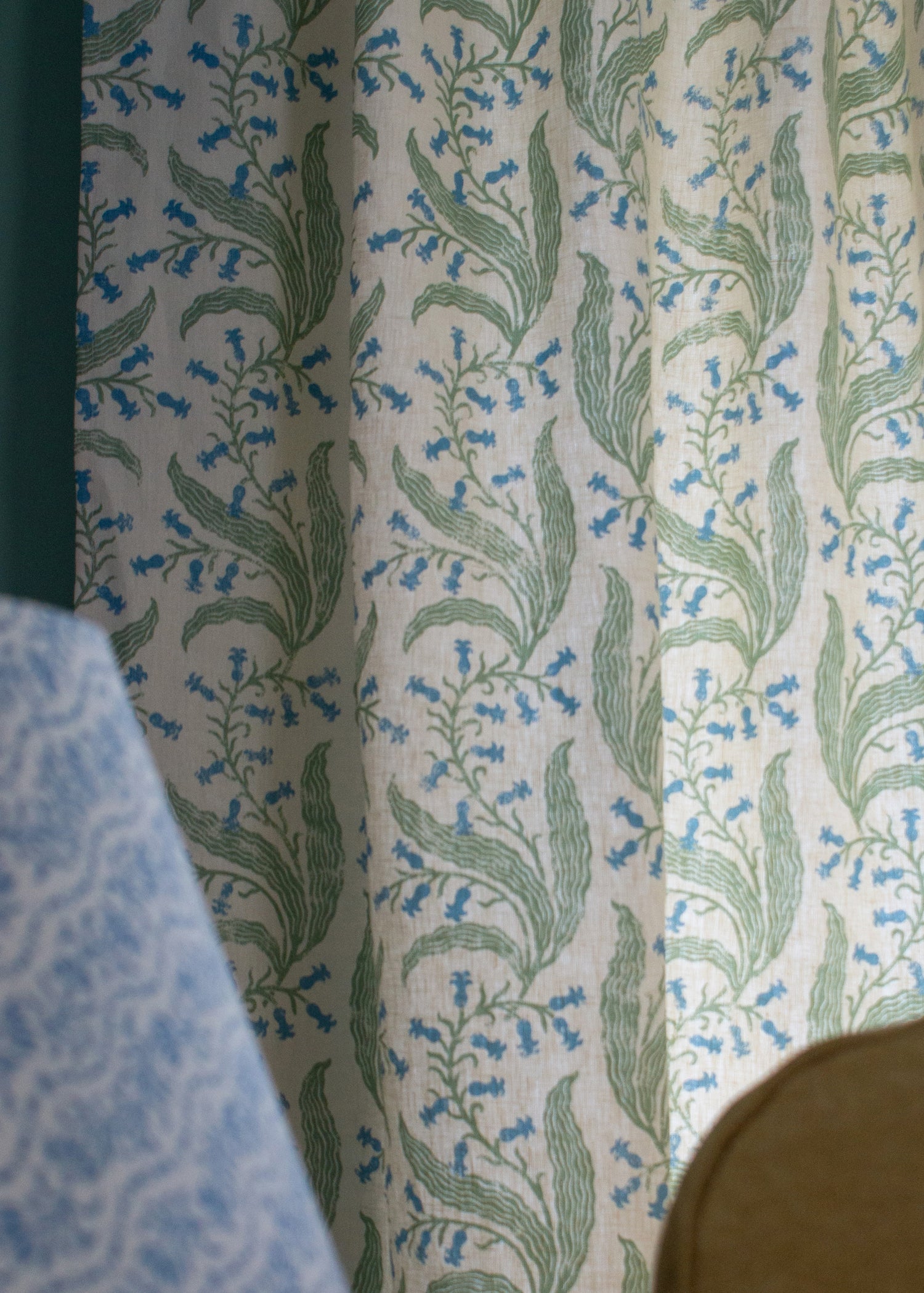 Detail of a curtain in a scrolling floral pattern in blue and green on a cream field. 