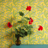 Teal table with vase and flowers against wallpaper in a scrolling floral pattern in blue and green on a yellow field. 