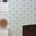 Wallpaper in a scrolling floral pattern in blue and green on a cream field surrounding a brick fireplace with a white bookshelf. 