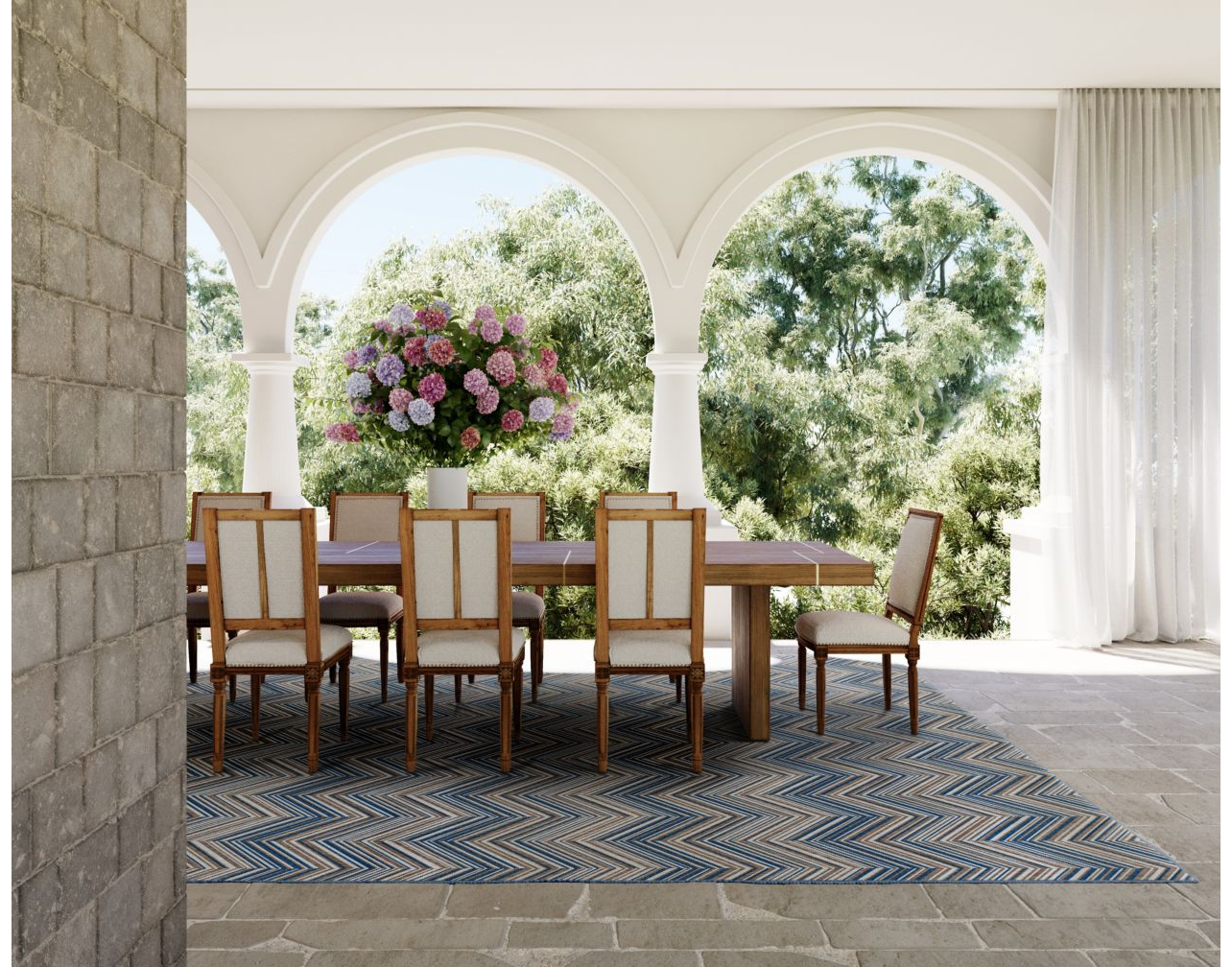 Outdoor dining room schene, with wooden table and chairs atop a blue and brown chevron area rug.