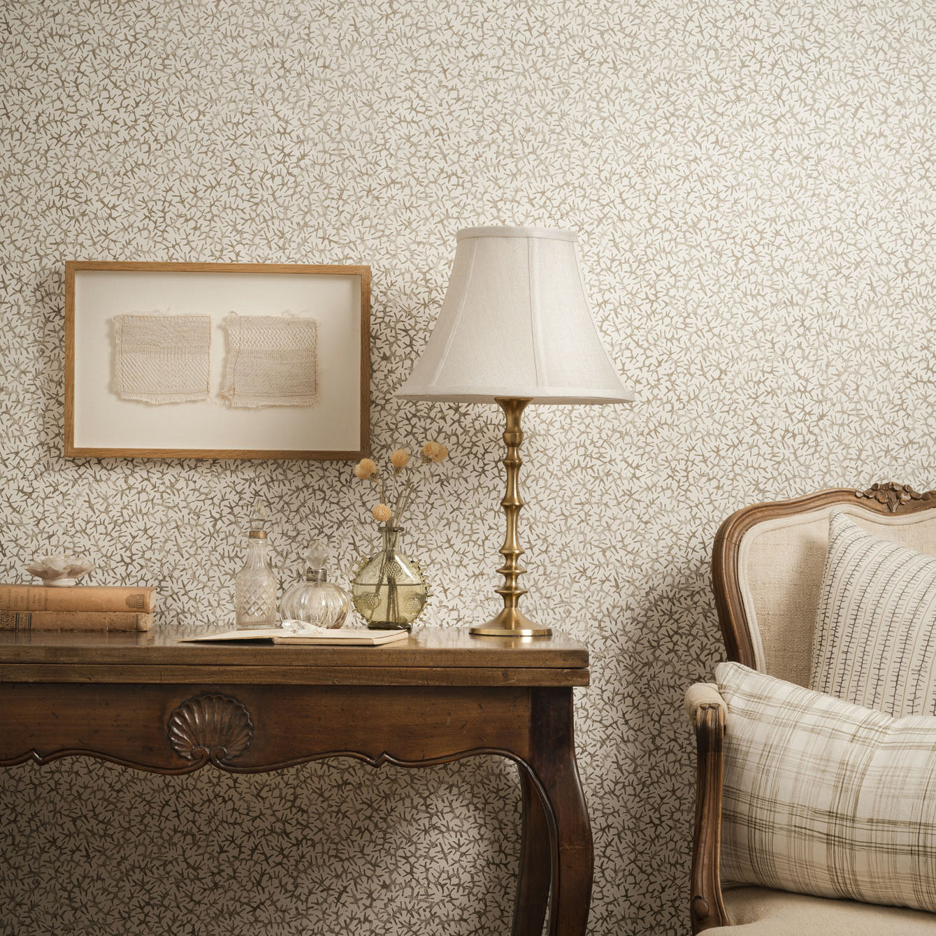 Living room scene with upholstered chair and wooden table with props against grey watercolor wallpaper. 