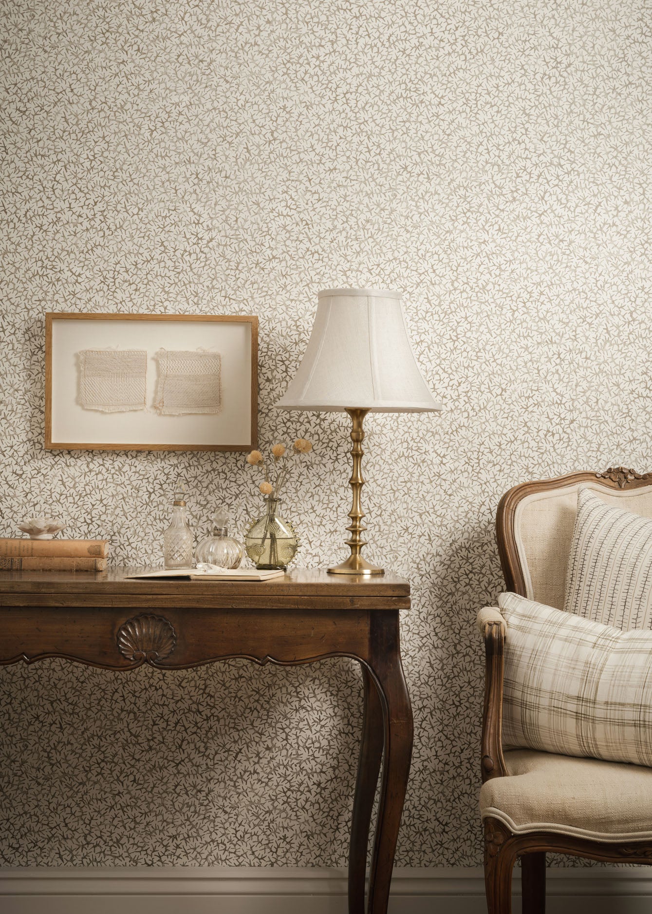 Living room scene with upholstered chair and wooden table with props against grey watercolor wallpaper. 