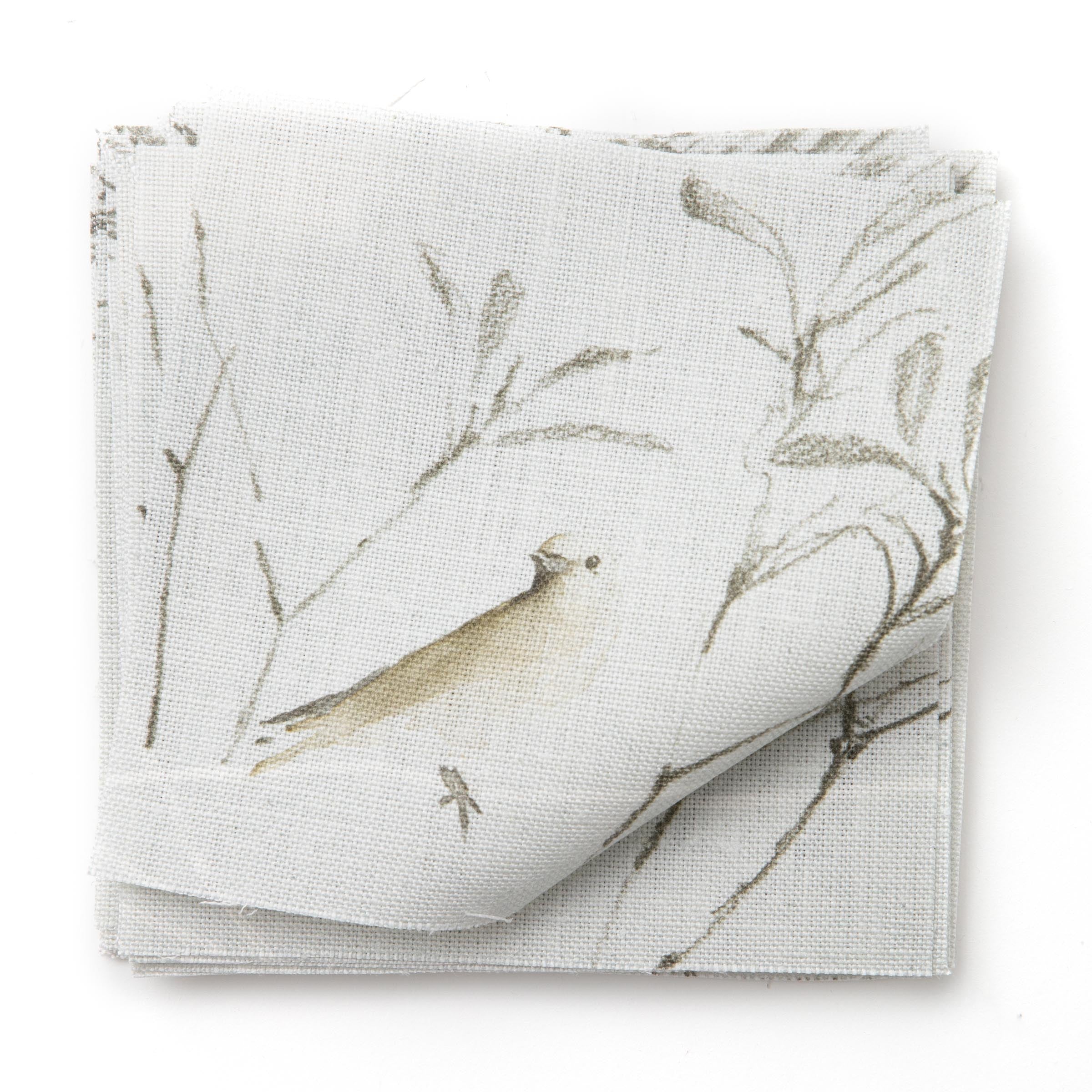 A stack of linen fabric swatches in a painterly bird and branch print in brown and gray on a light blue field.
