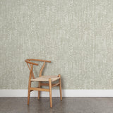 A wooden chair stands in front of a wall papered in a painterly dashed dot print in white on a pastel sage green field.