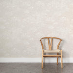 A wooden chair stands in front of a wall papered in a painterly cloud pattern in white on a soft beige field.