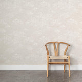 A wooden chair stands in front of a wall papered in a painterly cloud pattern in white on a soft beige field.