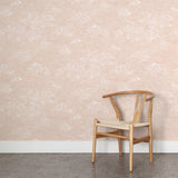 A wooden chair stands in front of a wall papered in a painterly cloud pattern in white on a pastel pink field.