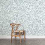 A wooden chair stands in front of a wall papered in a painterly branch print in white on a warm blue watercolor field.