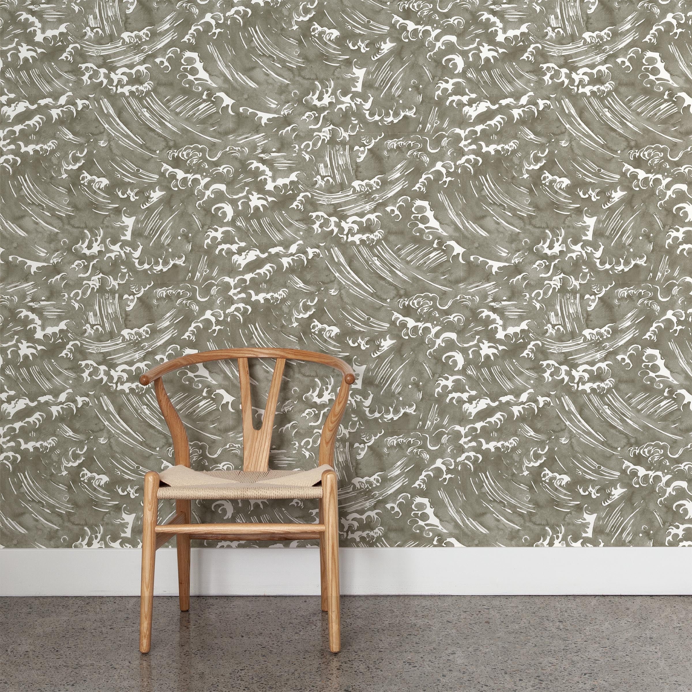 A wooden chair stands in front of a wall papered in a playful wave print in white on a grey watercolor field.
