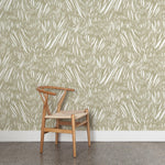 A wooden chair stands in front of a wall papered in an abstract leaf pattern in white on a sage green watercolor field.