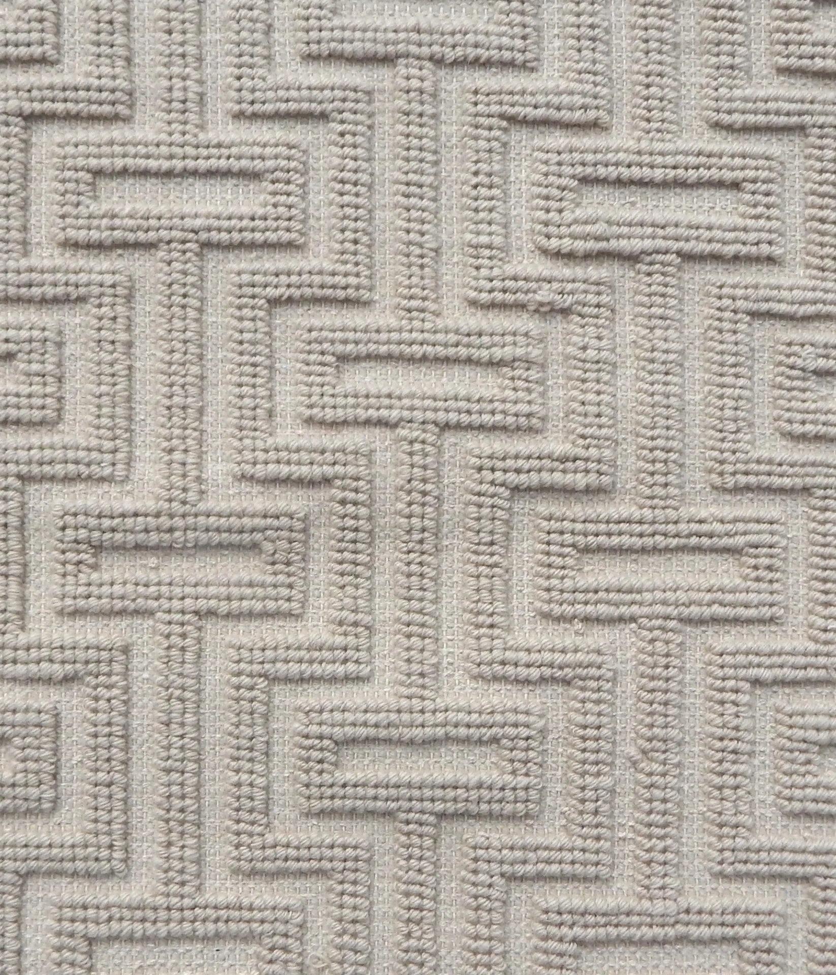 A close-up of a handwoven carpet with a repeating geometric maze in off white. 