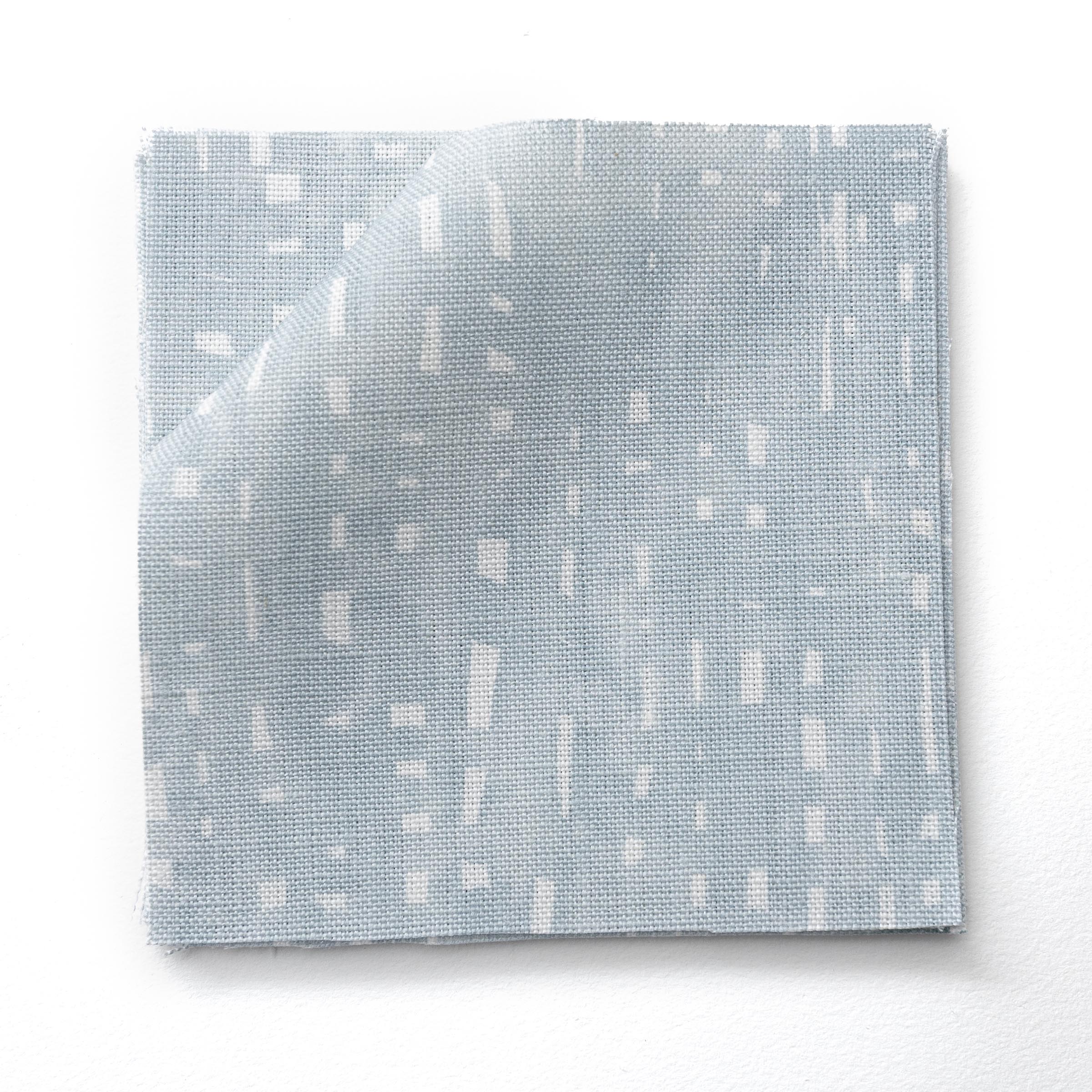 Stacked fabric swatches in a painterly small-scale dashed dot print in white on a soft blue watercolor field.