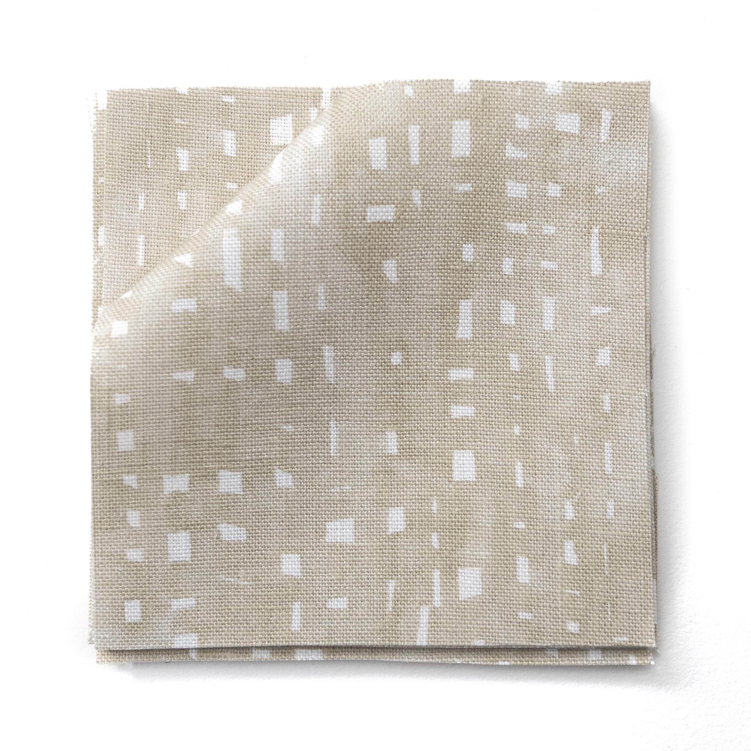 Stacked fabric swatches in a painterly small-scale dashed dot print in white on a soft taupe watercolor field.