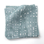 Stacked  fabric swatches in a painterly small-scale dashed dot print in white on a soft peacock blue watercolor field.