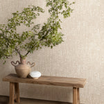 Wooden bench with urn and branches stands in front of a wall papered in a painterly dashed dot print in white on a soft beige field.