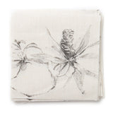 A stack of fabric swatches in a painterly pine cone and branch print in green on a cream field.