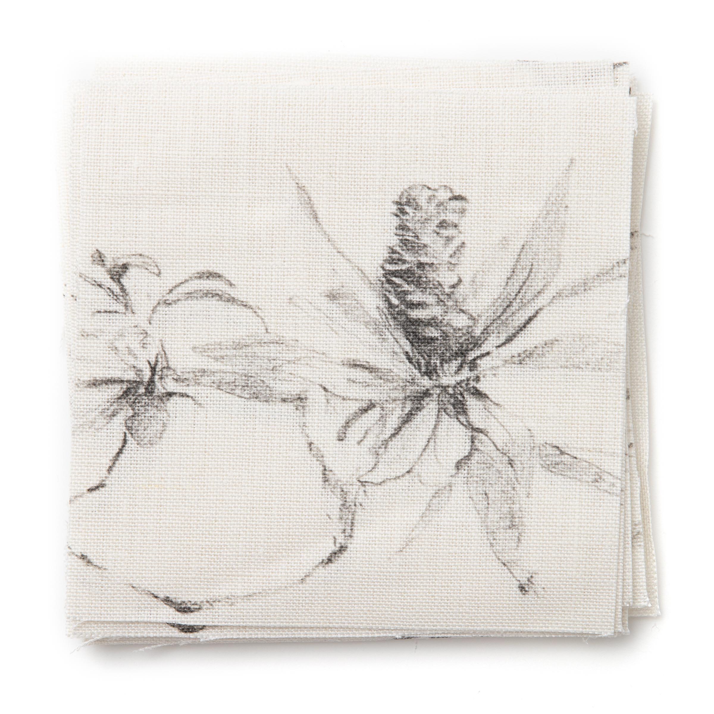 A stack of fabric swatches in a painterly pine cone and branch print in green on a cream field.