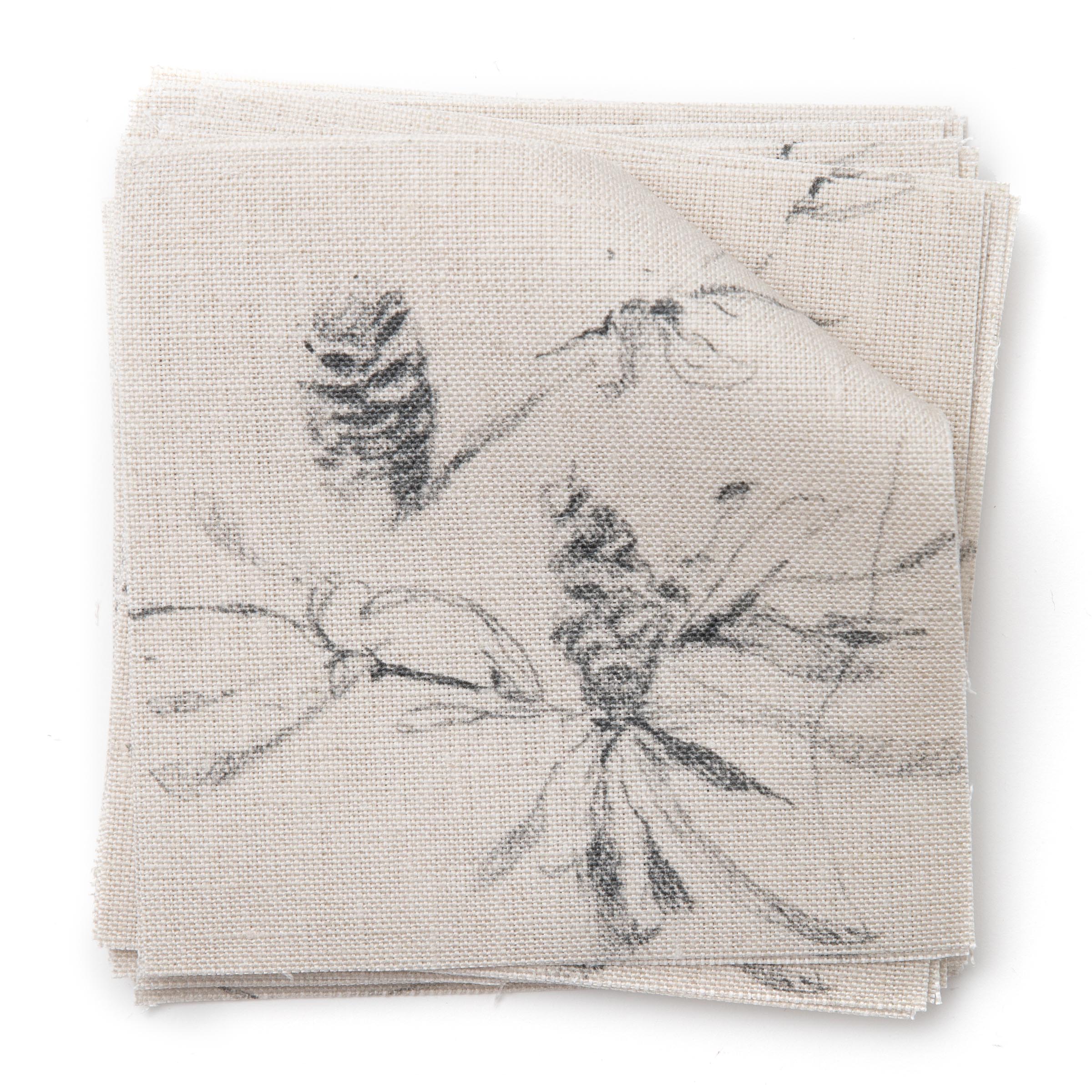 A stack of fabric swatches in a painterly pine cone and branch print in gray on a greige field.