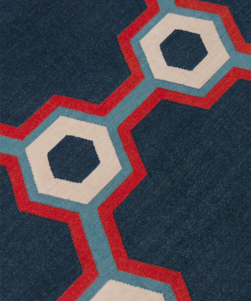 Detail of a flatwoven rug in a bold geometric floral-like design in blue, navy, red and cream. 