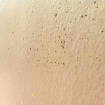 Wide-angle shot of wallpaper in a random splattered pattern in metallic gold on a cream field.