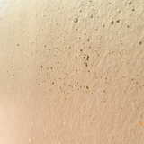 Wide-angle shot of wallpaper in a random splattered pattern in metallic gold on a cream field.