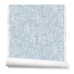 Partially unrolled wallpaper with a pattern of repeating watercolor illustrations of horses, farmers and country houses in white on a blue background.