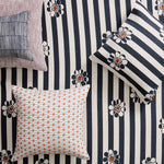 A styled flat-lay of throw pillows on fabric background with navy and white striped floral print, accompanied by four decorative throw pillows in different patterns.