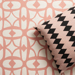 A close-up of a decorative throw pillow with a black and pink diamond stripe pattern, resting against a wallpaper with a pink and white lattice design.