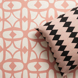 A close-up of a decorative throw pillow with a black and pink diamond stripe pattern, resting against a wallpaper with a pink and white lattice design.