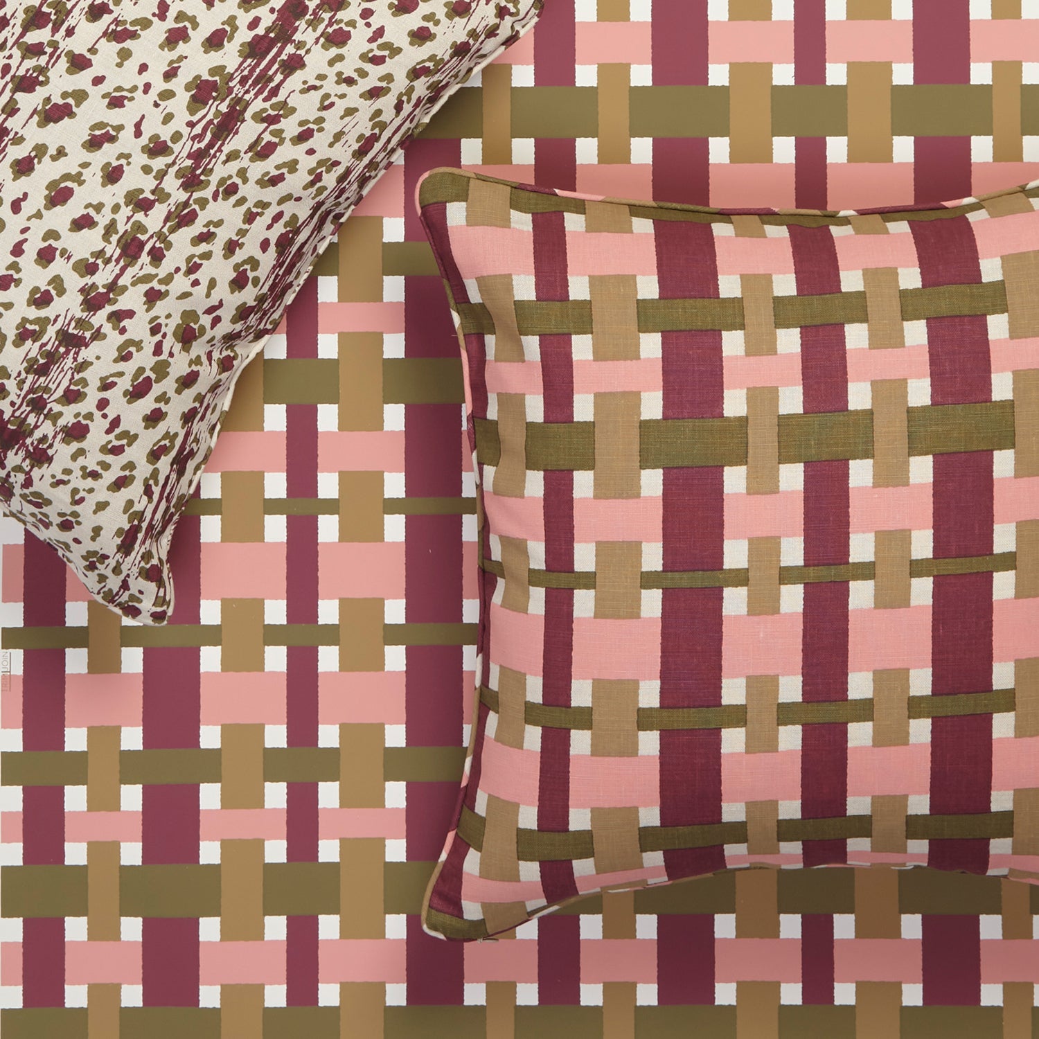 A close-up of a woven-texture throw pillow and matching pillowcase set on a bed. The pillow features a pink, burgundy, and olive green basketweave pattern, while the matching pillowcase has a leopard print design in cream and burgundy.