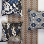 Three decorative throw pillows with navy, beige, and white patterns are arranged against a brown and white geometric patterned wallpaper. The pillows feature floral and abstract botanical designs in navy blue, beige, and white.