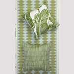 Two decorative throw pillows displayed against a patterned wallpaper background. The top pillow features a green and white tropical leaf print, and the bottom pillow has a textured green and white striped design.