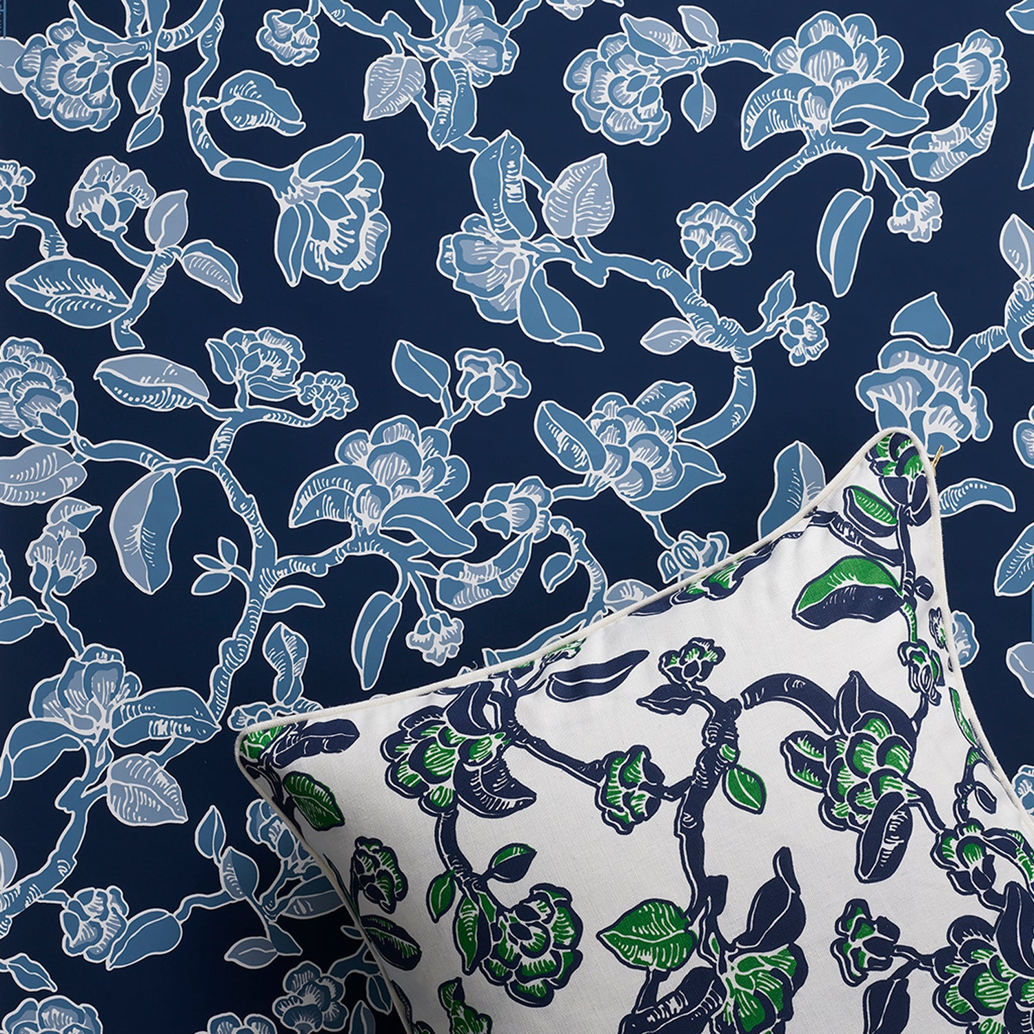 Styled flat-lay with throw pillow in a flower and branch pattern in blue and green on white against matching wallpaper in shades of blue. 