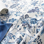 Blue and white floral patterned fabric with a rolled corner showing the backing, draped to display its texture and print.