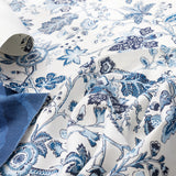Blue and white floral patterned fabric with a rolled corner showing the backing, draped to display its texture and print.