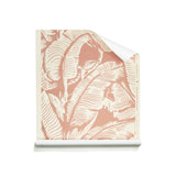 A roll of wallpaper with a tropical banana leaf pattern in dusty pink and cream, shown partially unrolled on a white background.