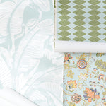 Three rolls of patterned wallpape, showing tropical leaf designs in pale mint and white, a green geometric diamond pattern on light blue, and a multicolor floral print on a pale blue background.